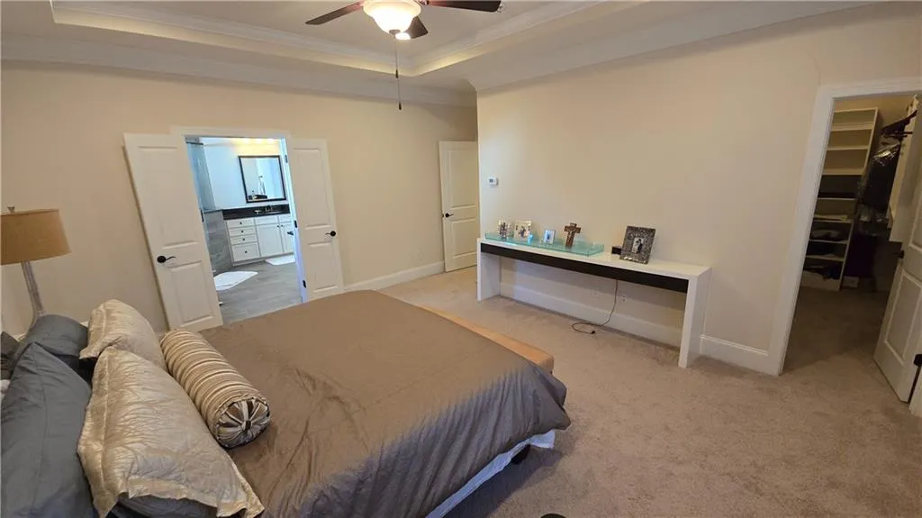 Bedroom with a walk in closet, a tray ceiling, crown molding, and light colored carpet