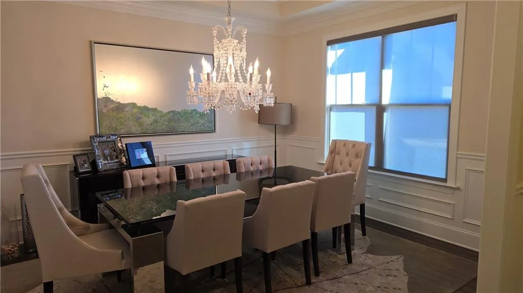 Dining room with a wainscoted wall, an inviting chandelier, ornamental molding, and a decorative wall