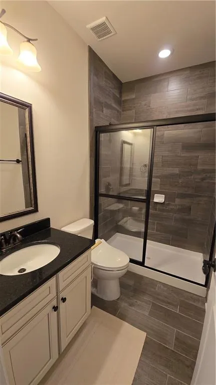 Bathroom featuring visible vents, a stall shower, toilet, and vanity