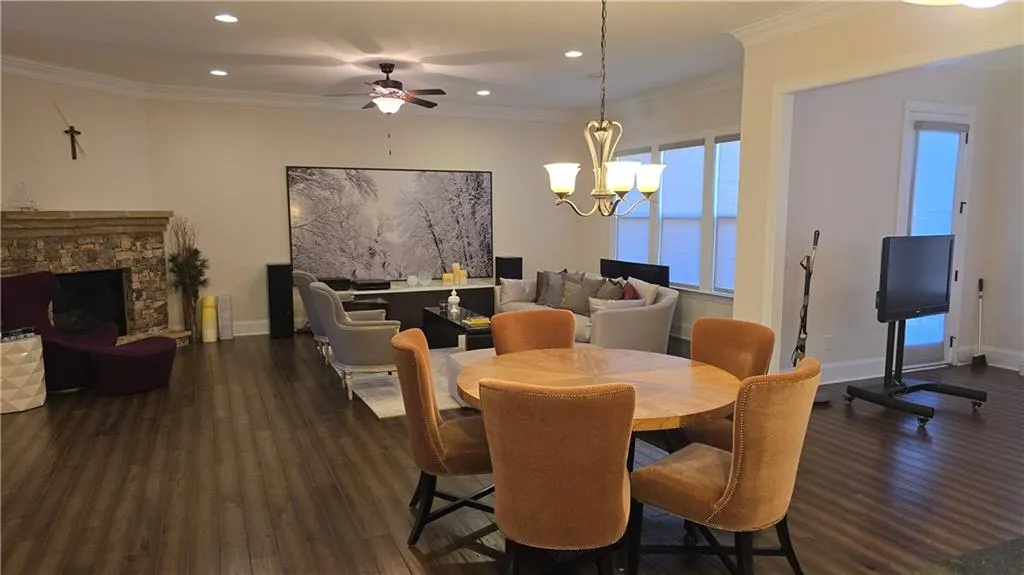 Dining area featuring ornamental molding, ceiling fan with notable chandelier, a fireplace, baseboards, and dark wood-style flooring