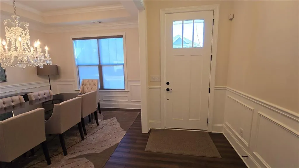 Entryway featuring a tray ceiling, dark wood-style flooring, ornamental molding, wainscoting, and a notable chandelier