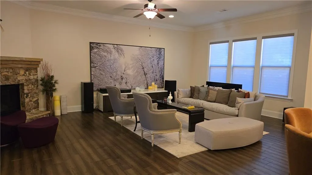 Living area featuring crown molding, baseboards, ceiling fan, a stone fireplace, and wood finished floors