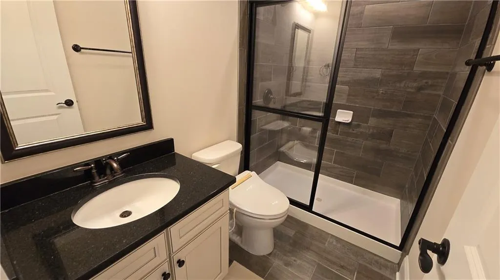 Full bath with toilet, tiled shower, and vanity