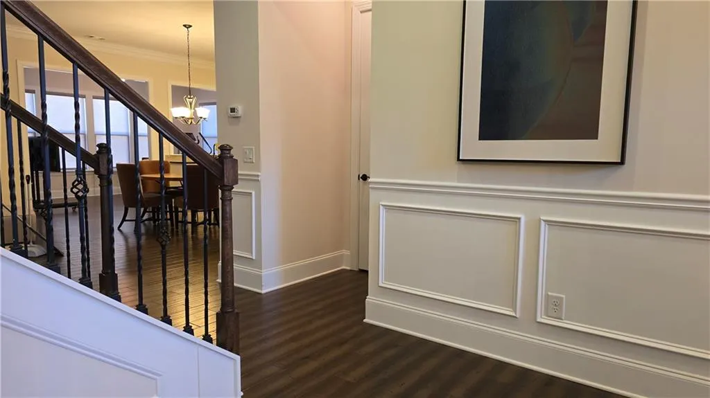 Staircase with a notable chandelier, ornamental molding, wood finished floors, wainscoting, and a decorative wall
