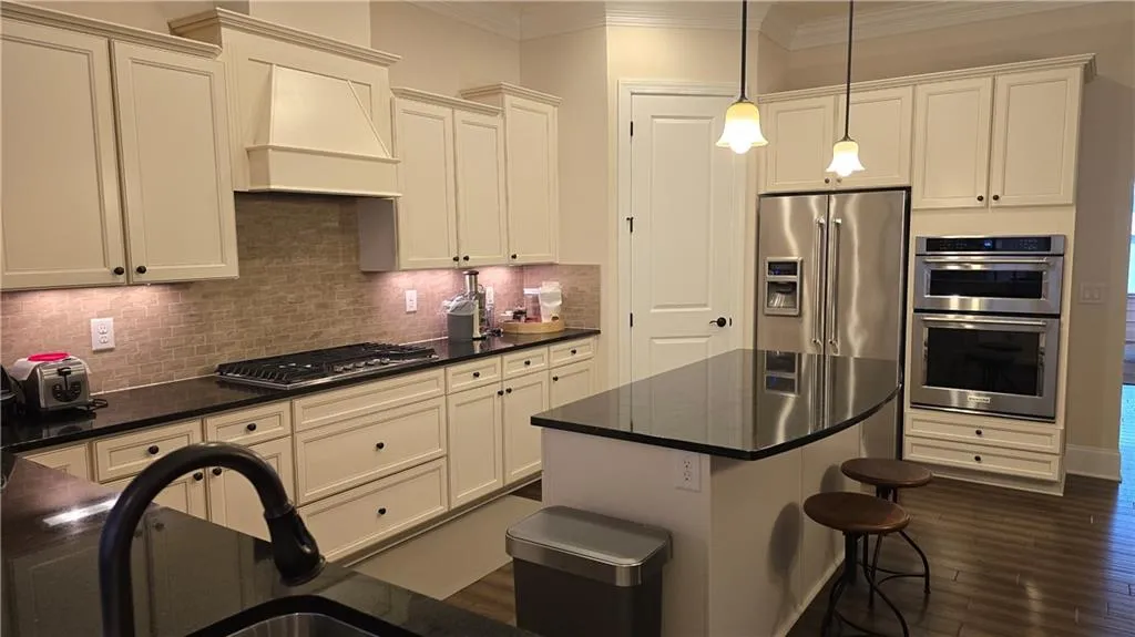 Kitchen with ornamental molding, decorative backsplash, custom range hood, appliances with stainless steel finishes, and dark countertops