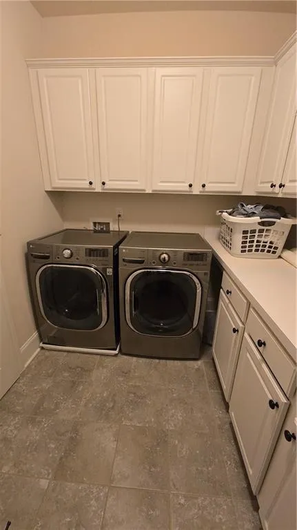 Clothes washing area featuring washer and dryer, cabinet space, and baseboards