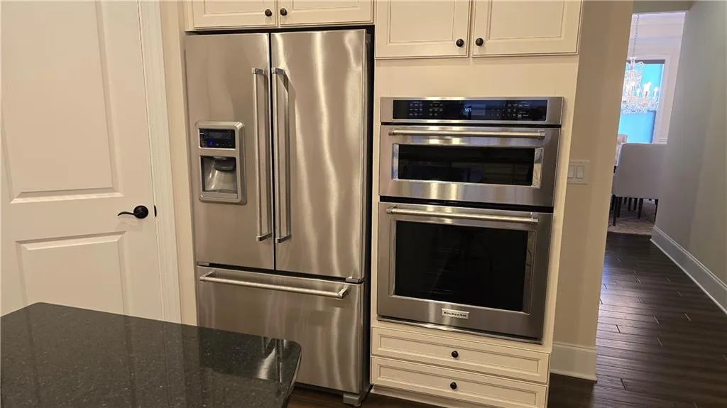 Kitchen featuring dark wood-type flooring, stainless steel appliances, dark stone counters, white cabinets, and baseboards