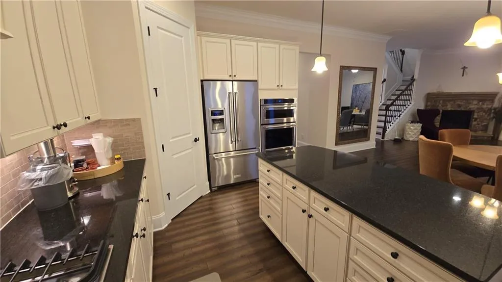 Kitchen featuring dark wood-type flooring, decorative light fixtures, ornamental molding, decorative backsplash, and stainless steel appliances