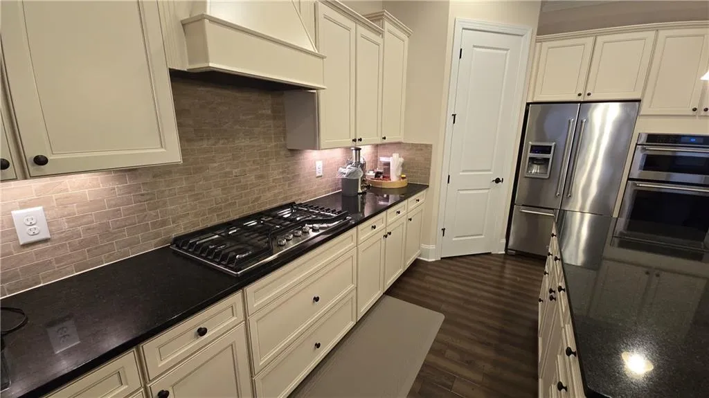 Kitchen featuring custom exhaust hood, dark wood-style flooring, stainless steel appliances, white cabinetry, and tasteful backsplash