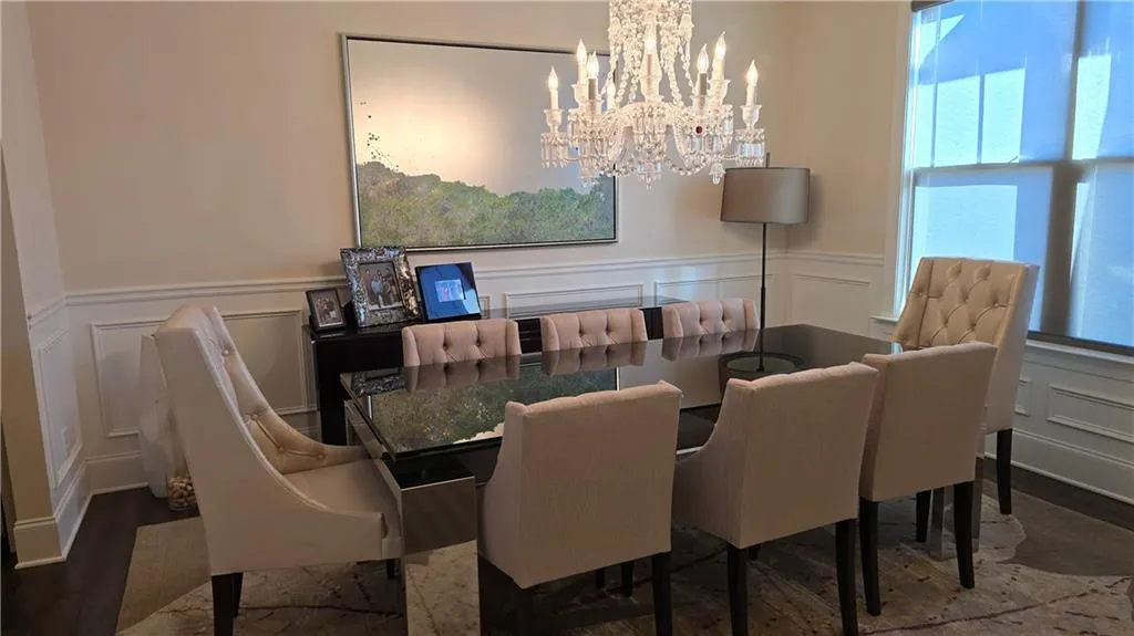 Dining room featuring a decorative wall, a notable chandelier, wood finished floors, and wainscoting