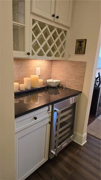 Bar featuring beverage cooler, baseboards, dark wood finished floors, decorative backsplash, and a dry bar