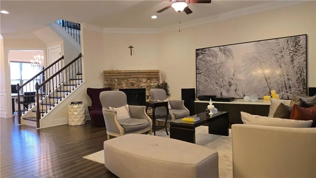 Living area featuring stairs, wood finished floors, ceiling fan with notable chandelier, and ornamental molding