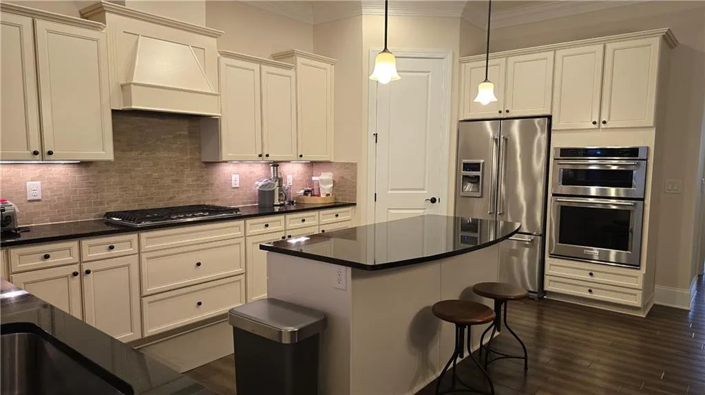 Kitchen featuring dark countertops, custom range hood, crown molding, and appliances with stainless steel finishes