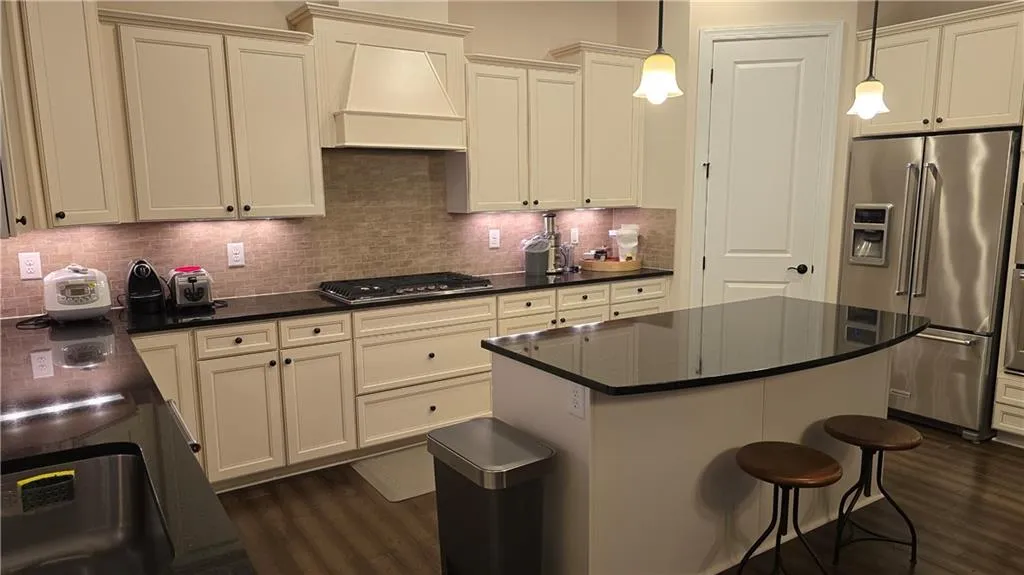 Kitchen with stainless steel appliances, tasteful backsplash, dark wood-style flooring, and custom range hood