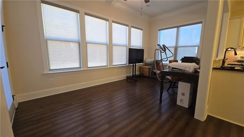 Office area featuring dark wood-type flooring, baseboards, crown molding, and a ceiling fan