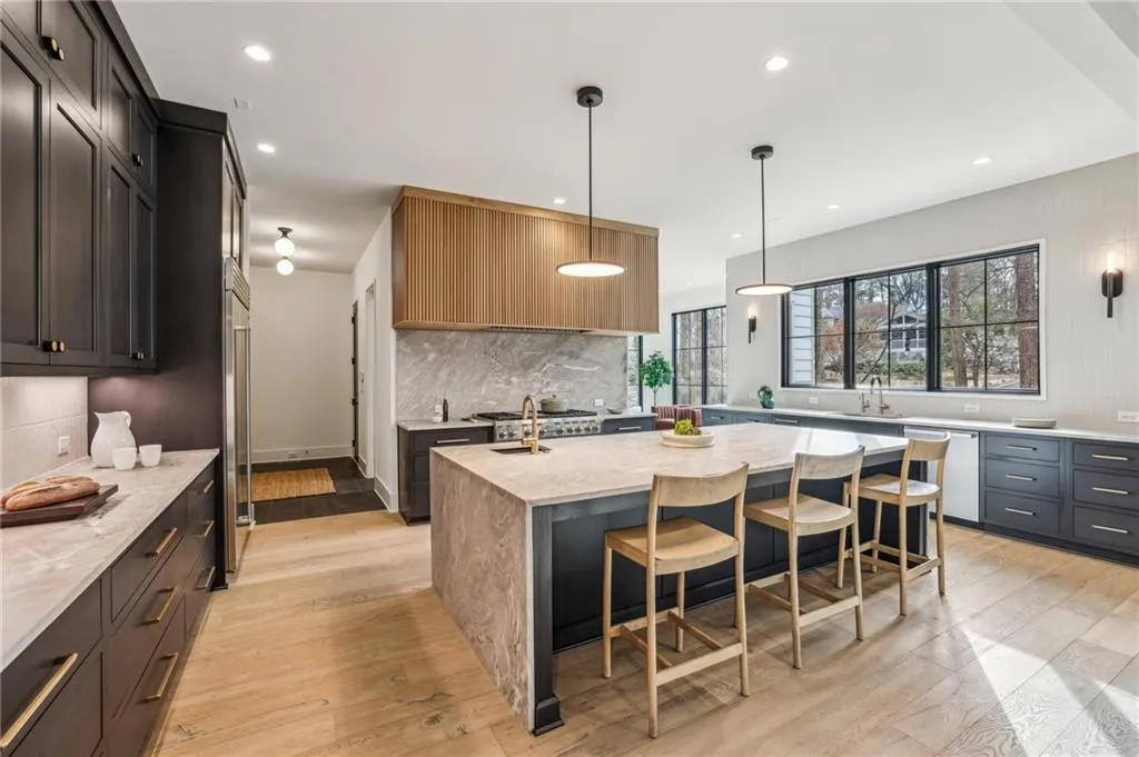 Kitchen with a breakfast bar area, appliances with stainless steel finishes, light stone countertops, a center island with sink, and decorative light fixtures