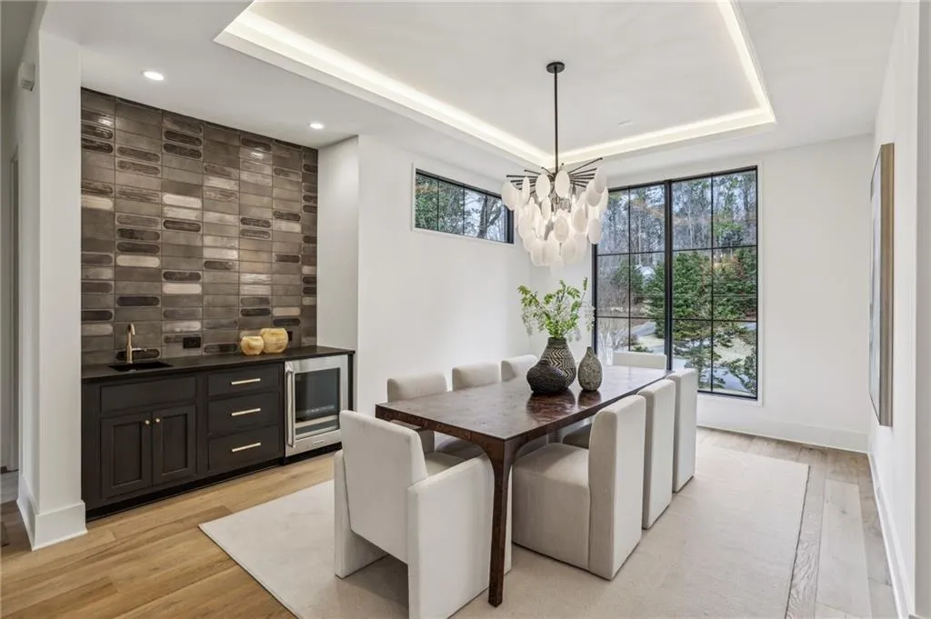 Dining room featuring sink, beverage cooler, a notable chandelier, a tray ceiling, and light hardwood / wood-style flooring