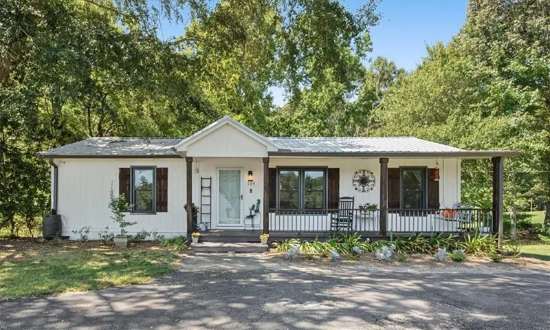 White horizontal siding exterior with a dark-stained wood porch, white vertical railing, and dark-framed windows with dark-stained wood shutters