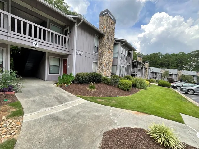 Stone facade accents, gray siding exterior, balconies with wood railings, landscaped grounds, and paved parking area