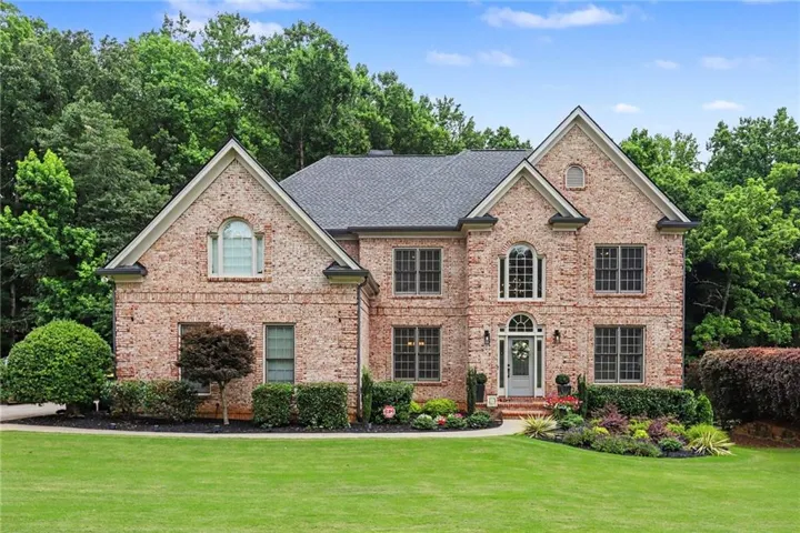 Traditional brick exterior with gabled rooflines, a prominent arched window above the entry, an arched transom window over the front door, dark shingle roofing, and established landscaping