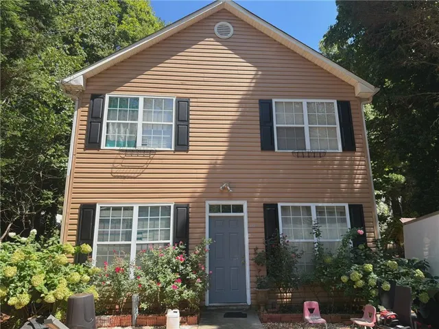 Two-story exterior with horizontal siding, multiple windows with black shutters, and a central entry door with a transom window
