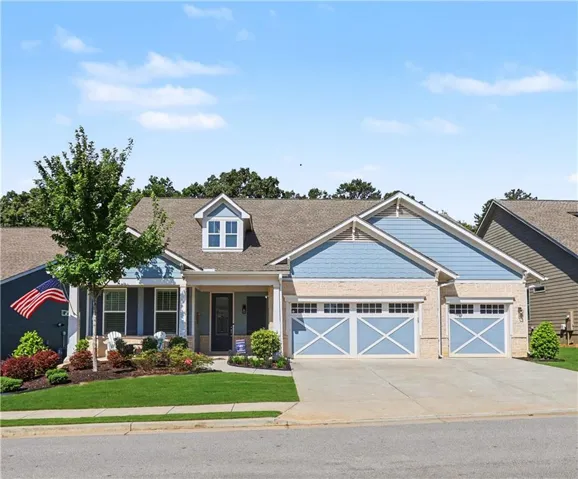 Blue siding exterior with a stone facade, featuring a covered front porch, dormer window, and an attached two-car garage with decorative doors