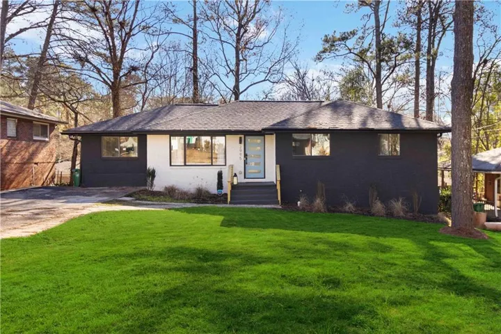 Modern ranch-style exterior featuring a striking black and white facade with black-framed windows, a light blue entry door with frosted glass, dark gray steps, and a lush green lawn