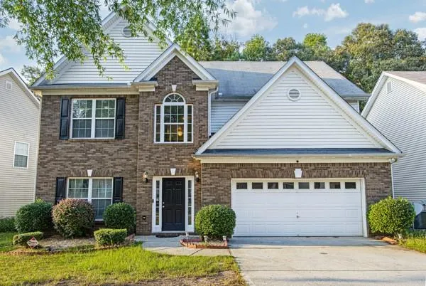 Brick and siding facade featuring a two-car garage, arched window, and landscaped front yard