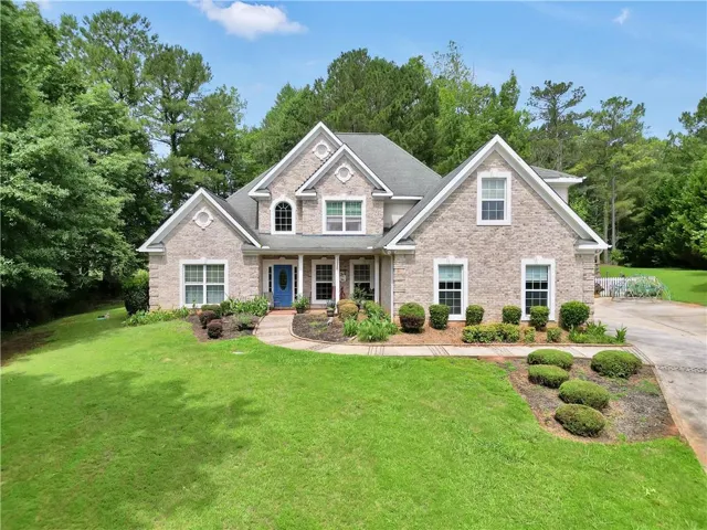 Two-story brick facade residence featuring a blue front door, gabled rooflines, multiple window styles, and a paved driveway