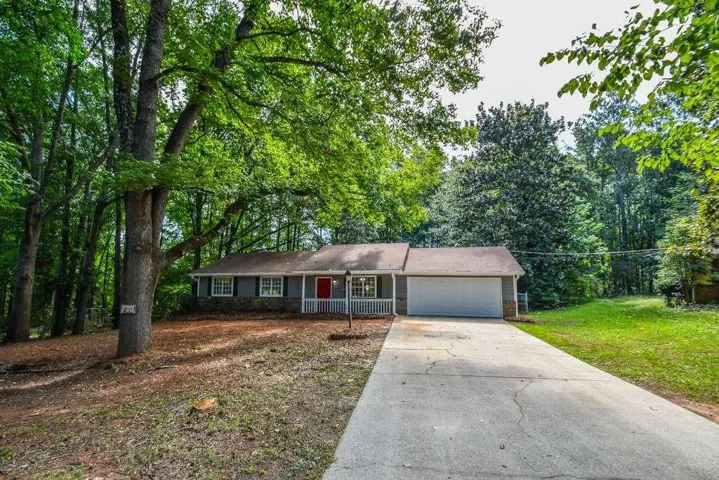 Ranch-style residence featuring a red front door, covered porch with white railing, and a two-car garage