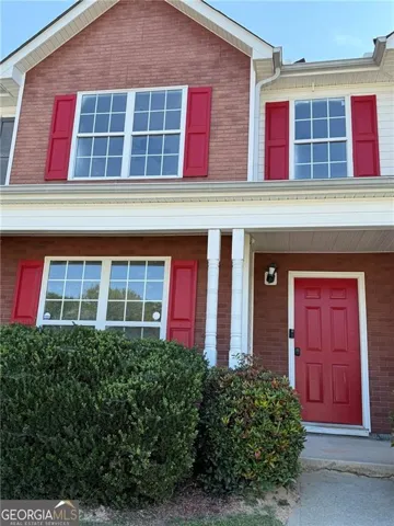 Brick façade with white trim, red paneled door, and red window shutters