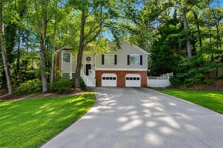 Two-story residence featuring a two-car garage with white paneled doors, gray siding, and a brick base