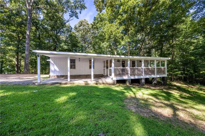 White board and batten siding, covered front porch, gravel driveway, wood railing, mature trees