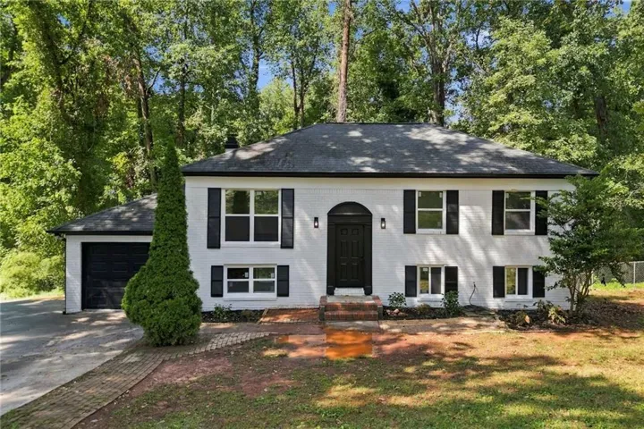 White brick exterior with black shutters, arched front entry, black garage door, and mature trees