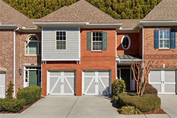 View of front facade featuring driveway, brick siding, a shingled roof, and an attached garage