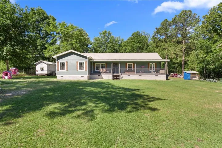 Single-story residence featuring light gray siding, a metal roof, a covered front porch, and a spacious front lawn
