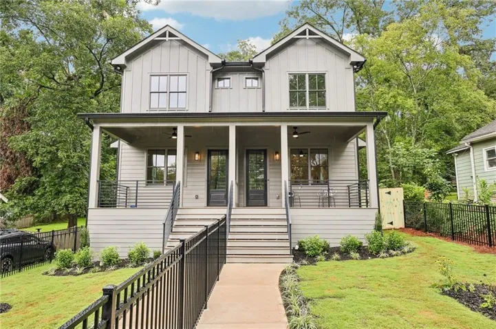 Modern farmhouse duplex featuring vertical and horizontal siding, covered front porches with ceiling fans, black frame windows, and a black wrought iron fence