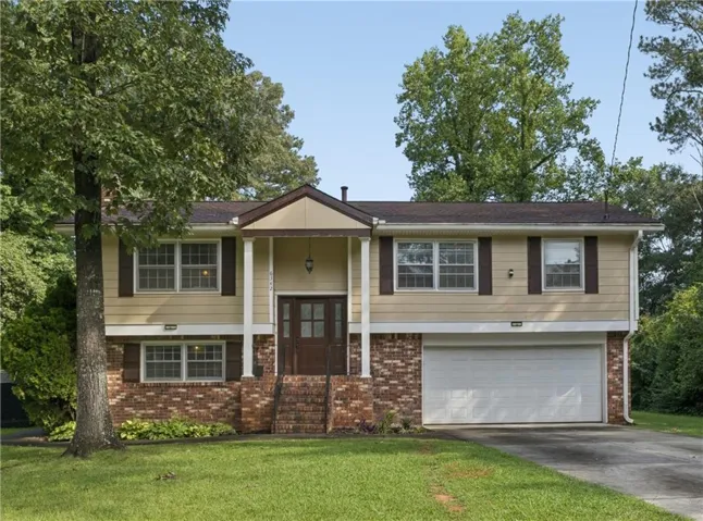 Split-level residence featuring a brick and siding exterior, a covered entryway with pillars, and a two-car garage