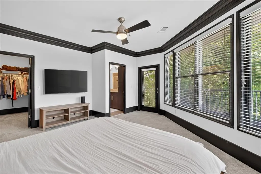 Bedroom with ornamental molding, light carpet, a spacious closet, ceiling fan, and ensuite bath