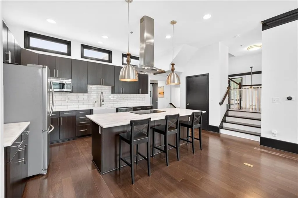 Kitchen with backsplash, a center island with sink, stainless steel appliances, a kitchen bar, and hanging light fixtures