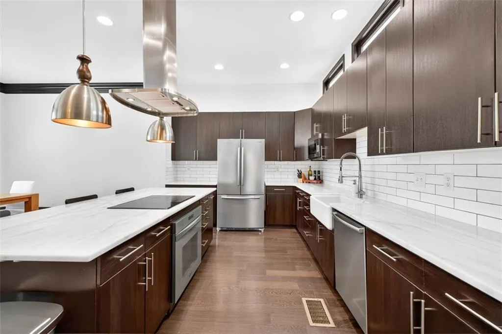Kitchen featuring a kitchen bar, dark brown cabinetry, appliances with stainless steel finishes, pendant lighting, and decorative backsplash