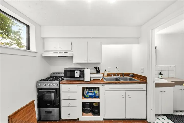 Compact kitchen featuring a gas range, white cabinetry, wood-finish countertops, a double basin sink, and a high window