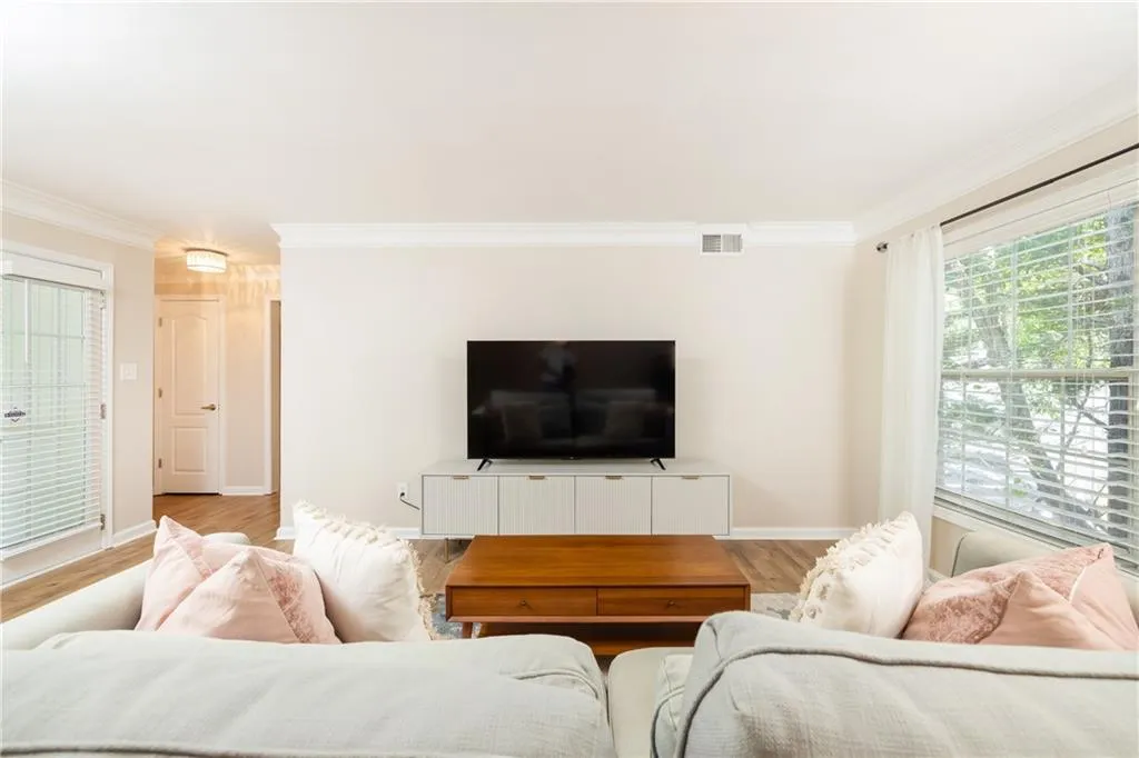 Living area featuring wood-finish flooring, a contemporary media console, and a large window with horizontal blinds