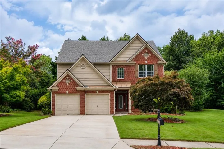 Traditional brick and siding exterior with a two-car garage, concrete driveway, and established landscaping