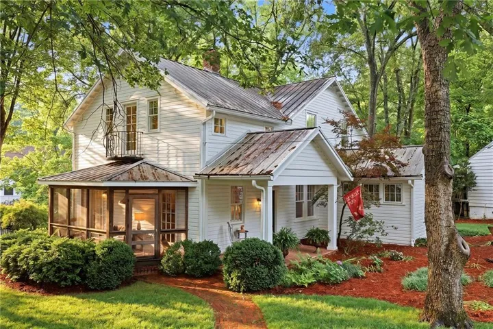 White clapboard exterior with a metal roof, featuring a screened-in porch with a separate balcony above
