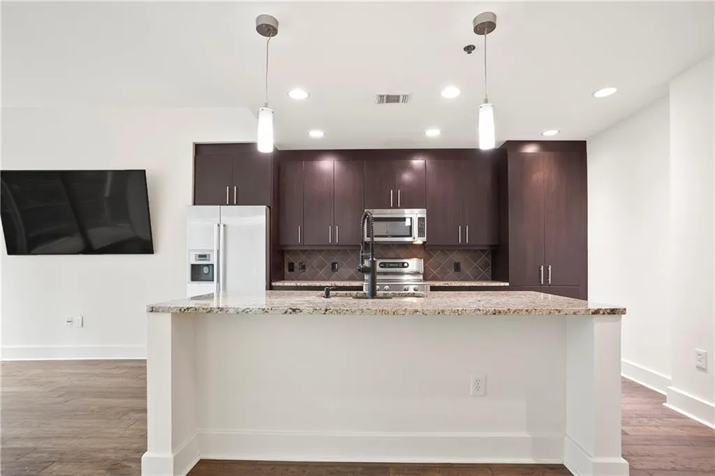 Kitchen featuring high end refrigerator, stainless steel microwave, backsplash, an island with sink, and dark brown cabinets