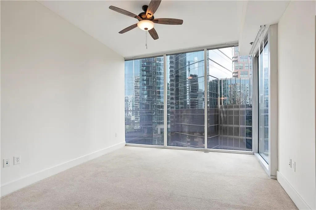 Carpeted spare room with a ceiling fan, expansive windows, and a city view