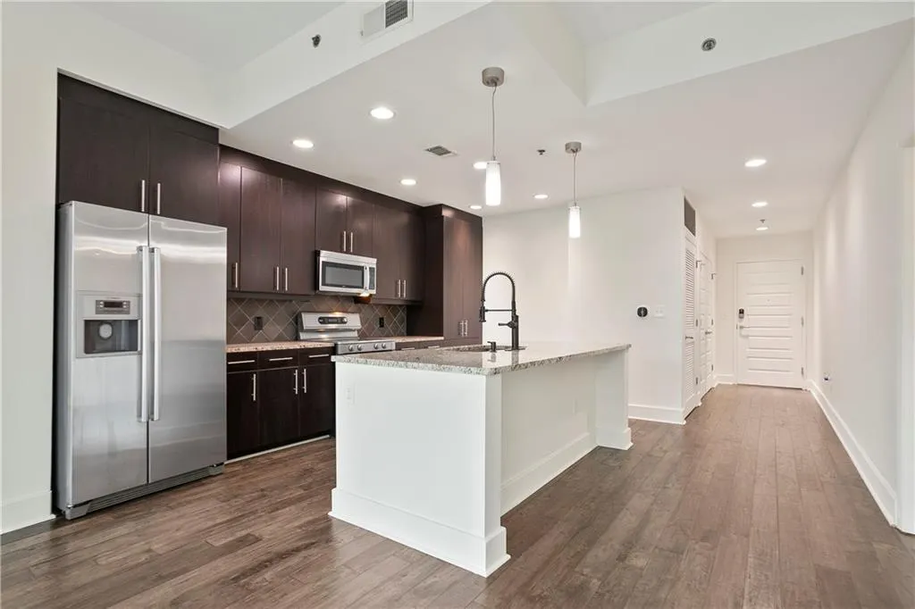 Kitchen with stainless steel appliances, dark wood-style floors, tasteful backsplash, a center island with sink, and recessed lighting
