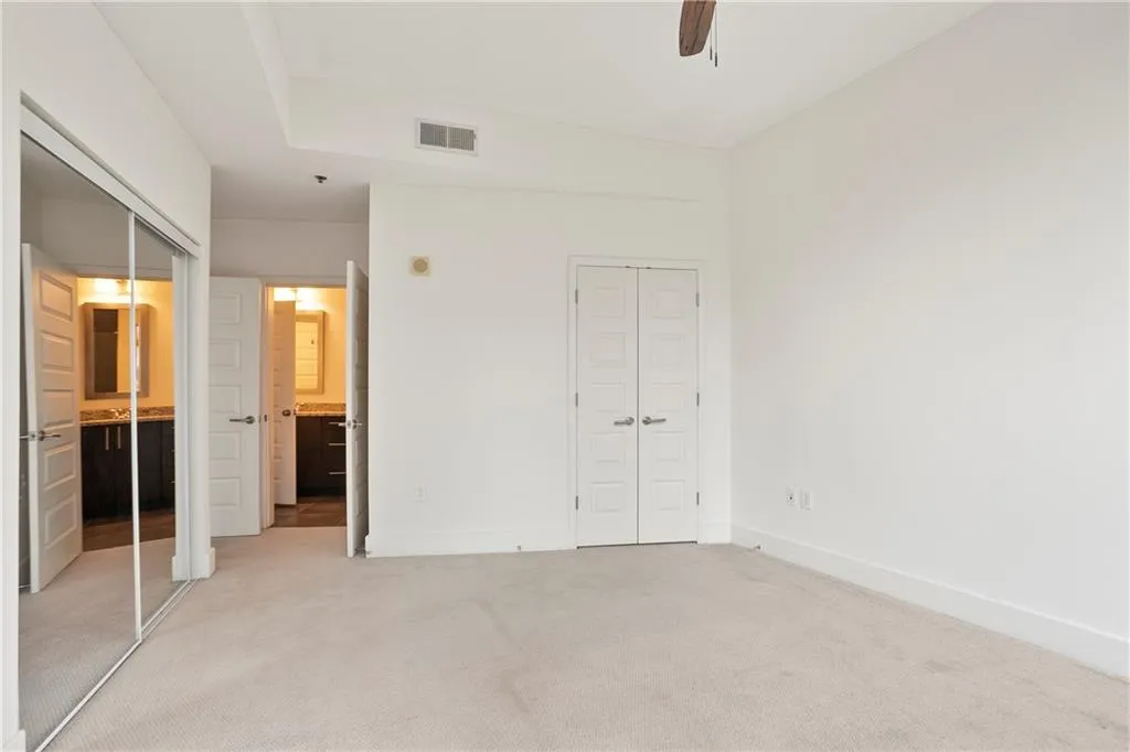 Unfurnished bedroom featuring light colored carpet, ensuite bathroom, and ceiling fan