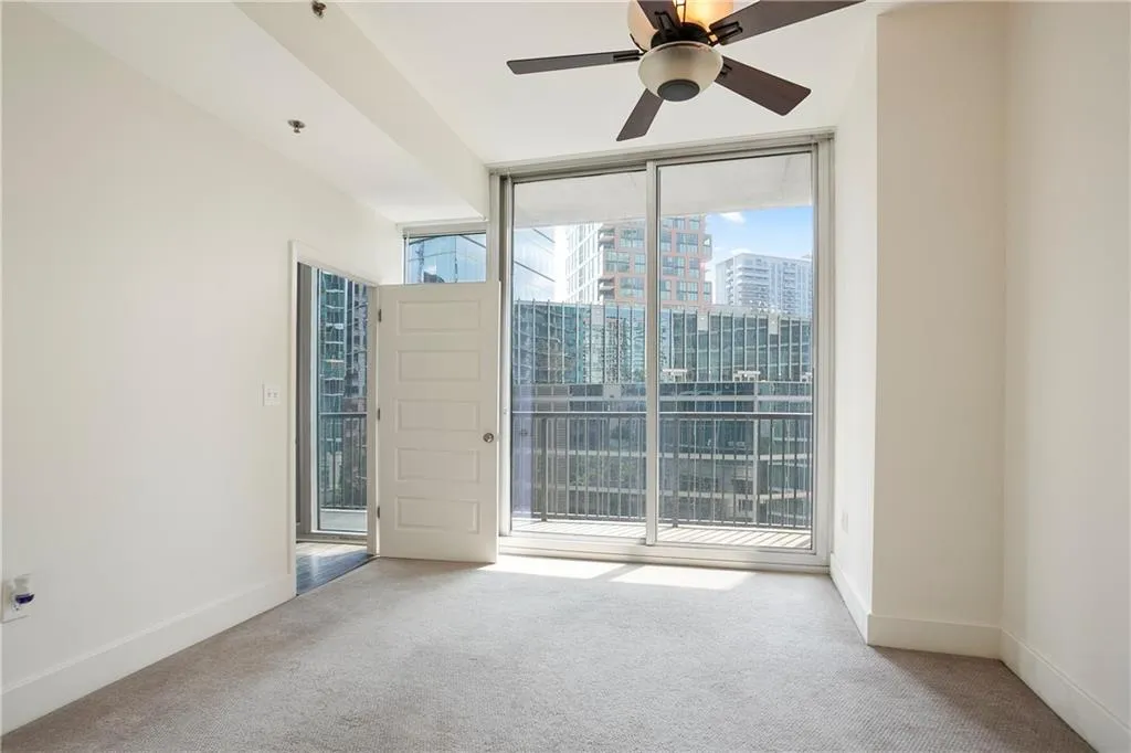 Empty room with floor to ceiling windows, carpet floors, ceiling fan, and a city view
